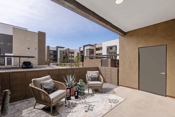 A patio with two chairs, a table, and a rug with a cactus and vase on it.